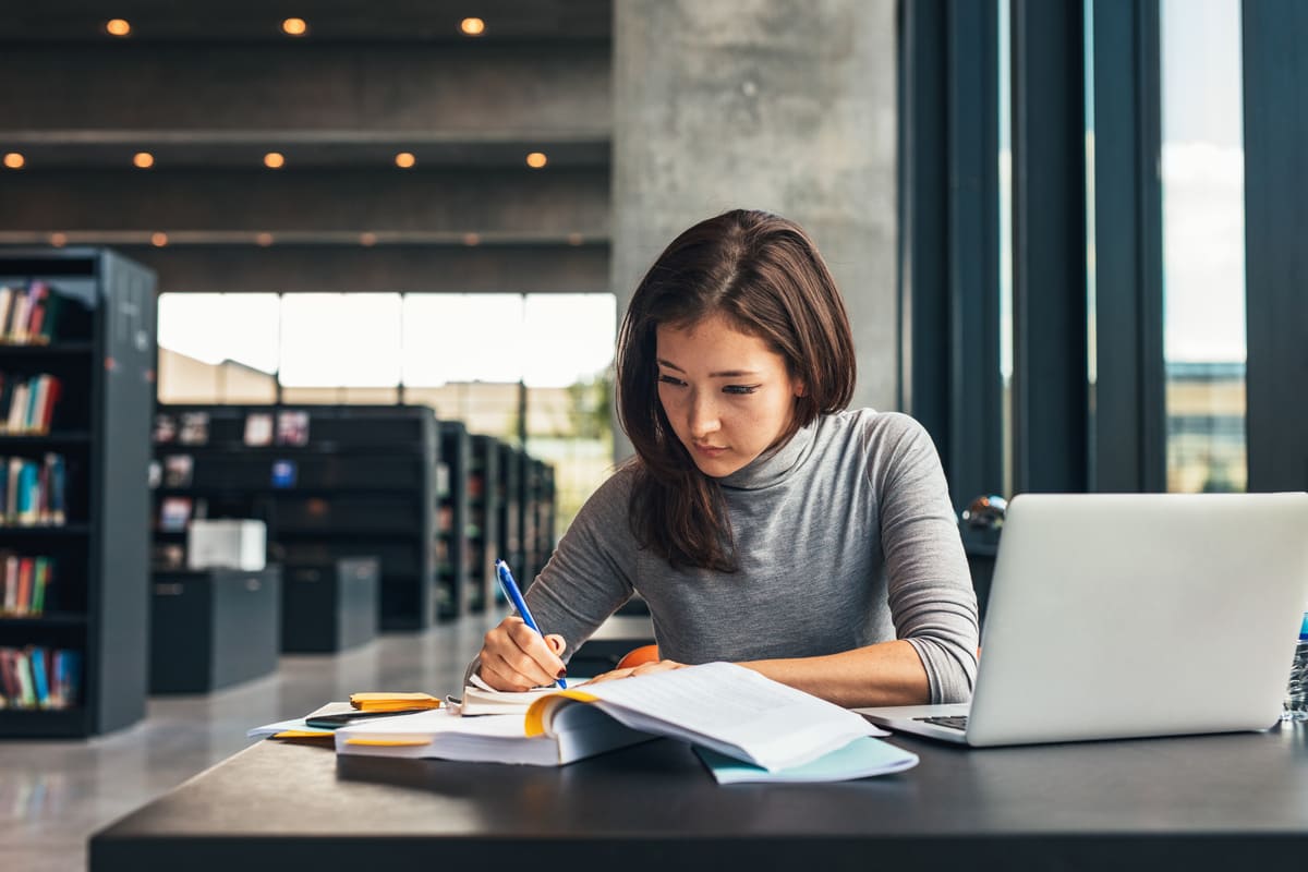 Mulher estudando com livros e notebook em uma mesa de biblioteca