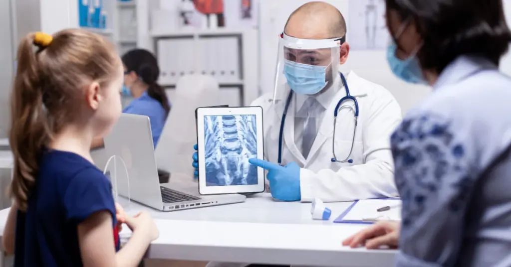 Cirurgião pediátrico analisando radiografia em um tablet junto com uma menina paciente e sua mãe